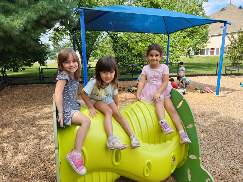 3 Girls smiling and playing in a playground at St Timothy's Preeschool
